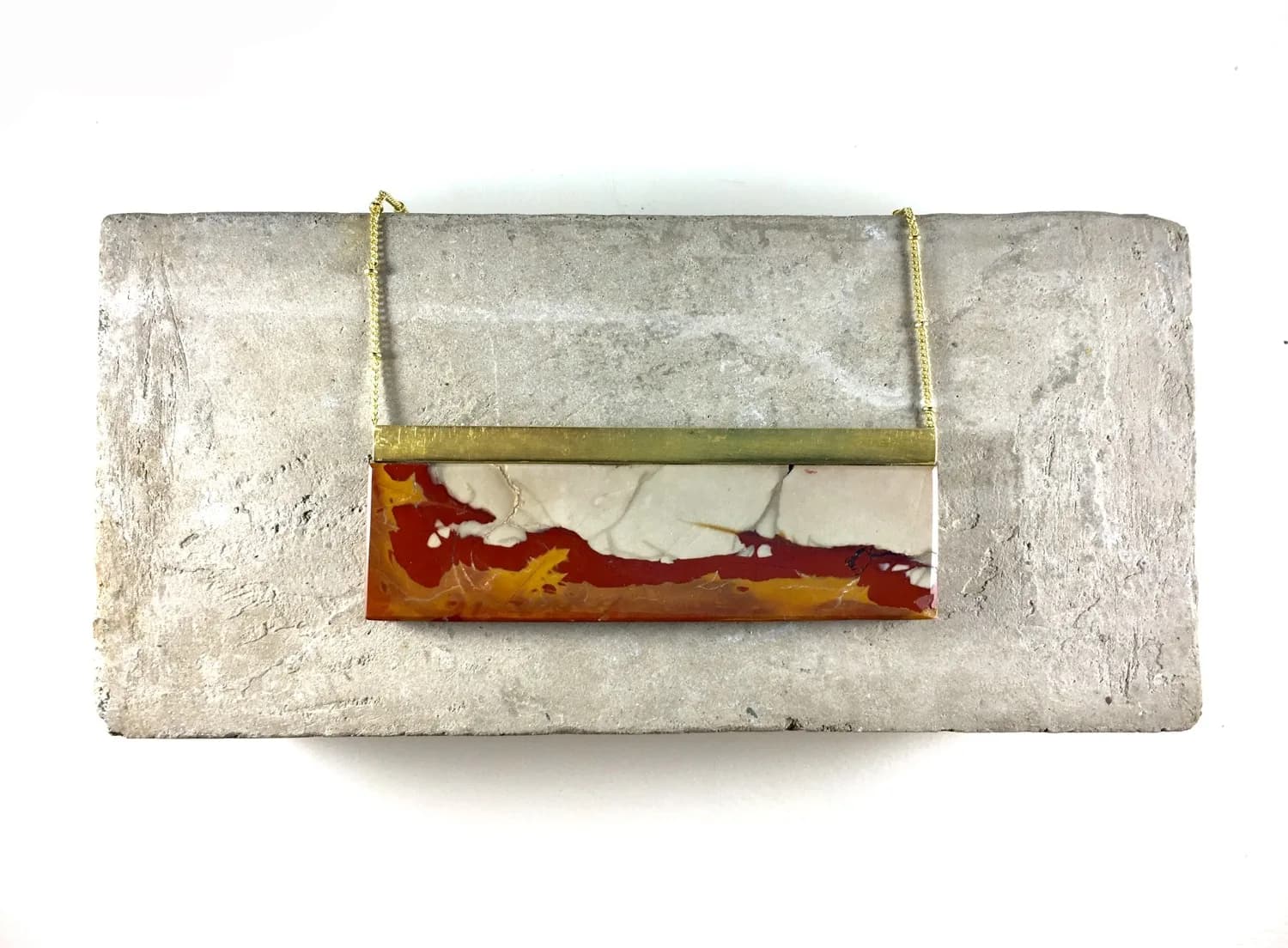 A striking necklace features a rectangular stone pendant with red and cream marbling, suspended from a gold chain and frame.