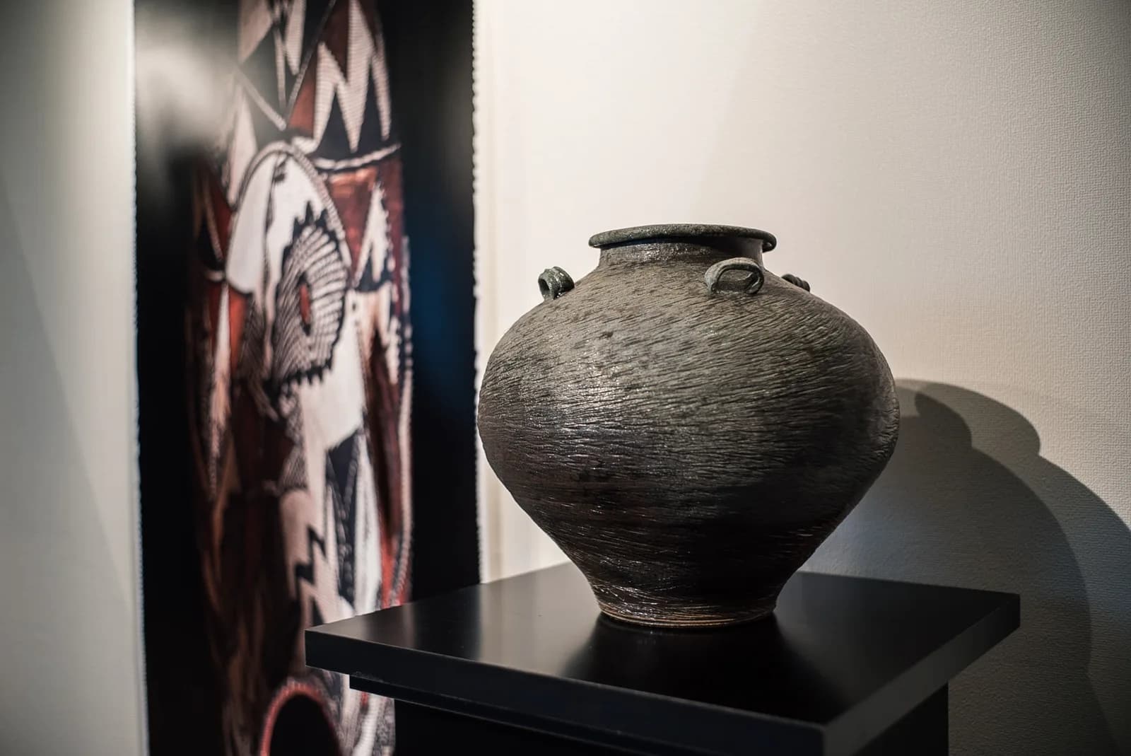 A textured ceramic vase with handles sits on a black pedestal, rendered in shades of Bunker and Schooner.