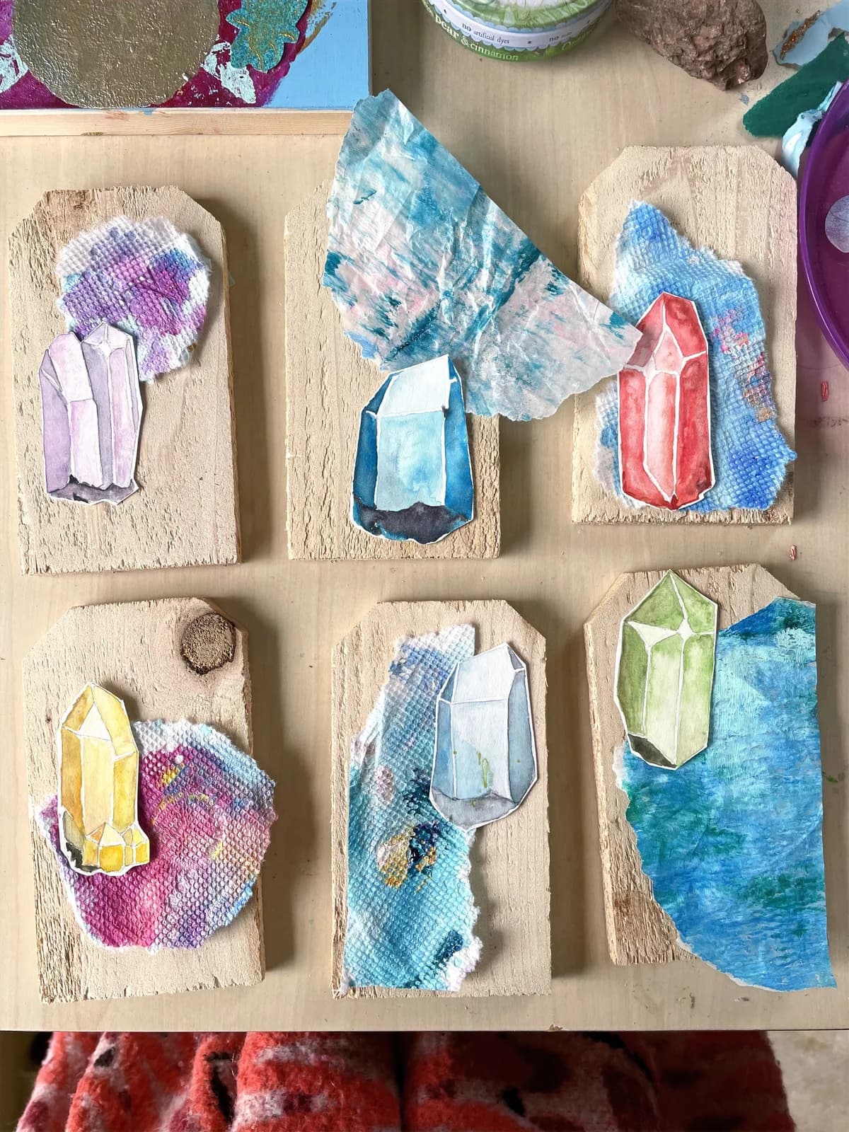 A collection of art tags featuring watercolor crystals and torn paper on wooden bases.