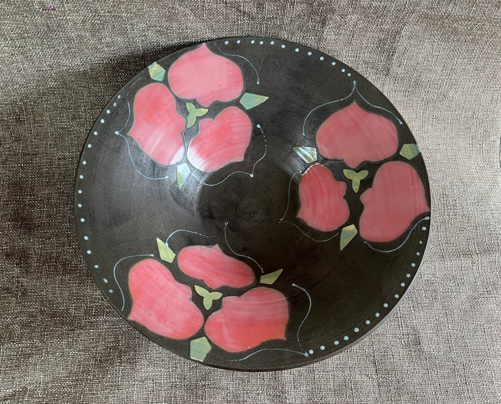 A dark ceramic bowl decorated with pink floral motifs and a dotted border.