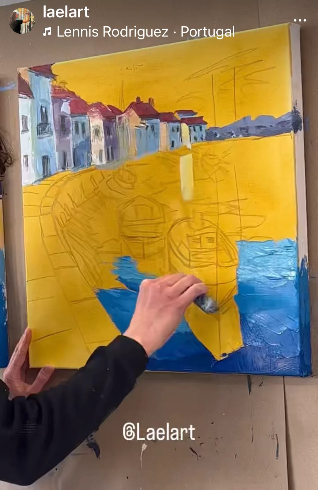 An artist's hands apply yellow and blue paint to a canvas depicting a coastal scene with boats.