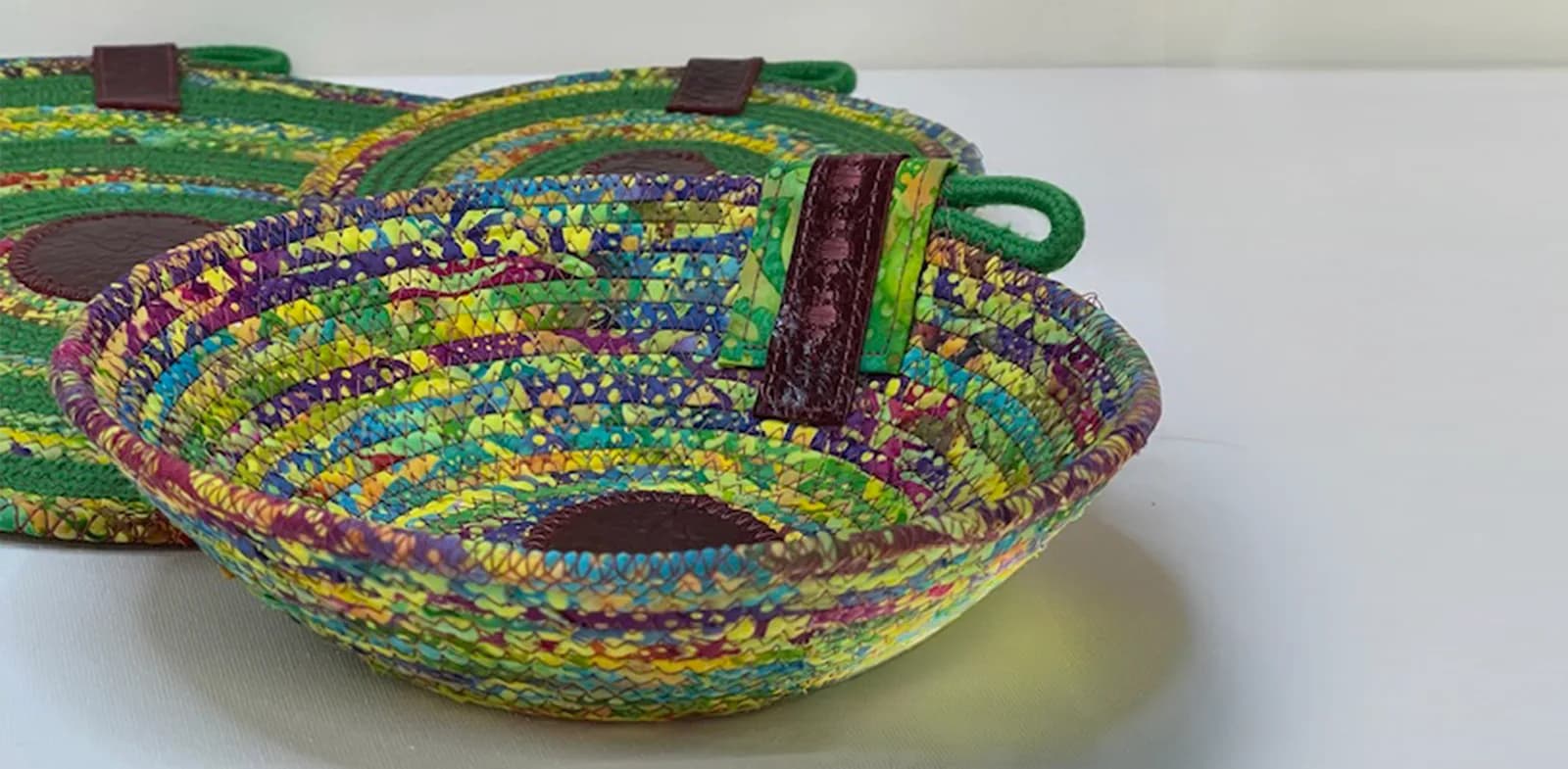 A colorful fabric rope bowl with leather accents is displayed on a white surface.