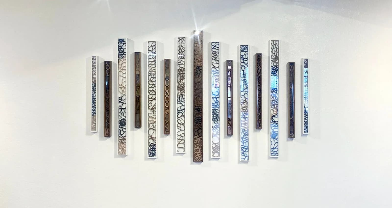 A collection of abstract metal wall sculptures with intricate cut-out patterns in shades of Cararra, Celeste, and Silver Sand.