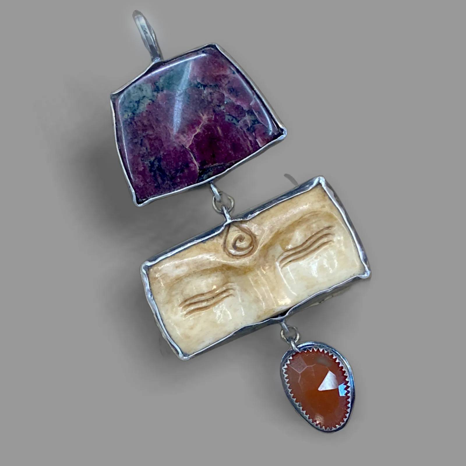 A unique pendant featuring a carved face and gemstones, crafted from metal.