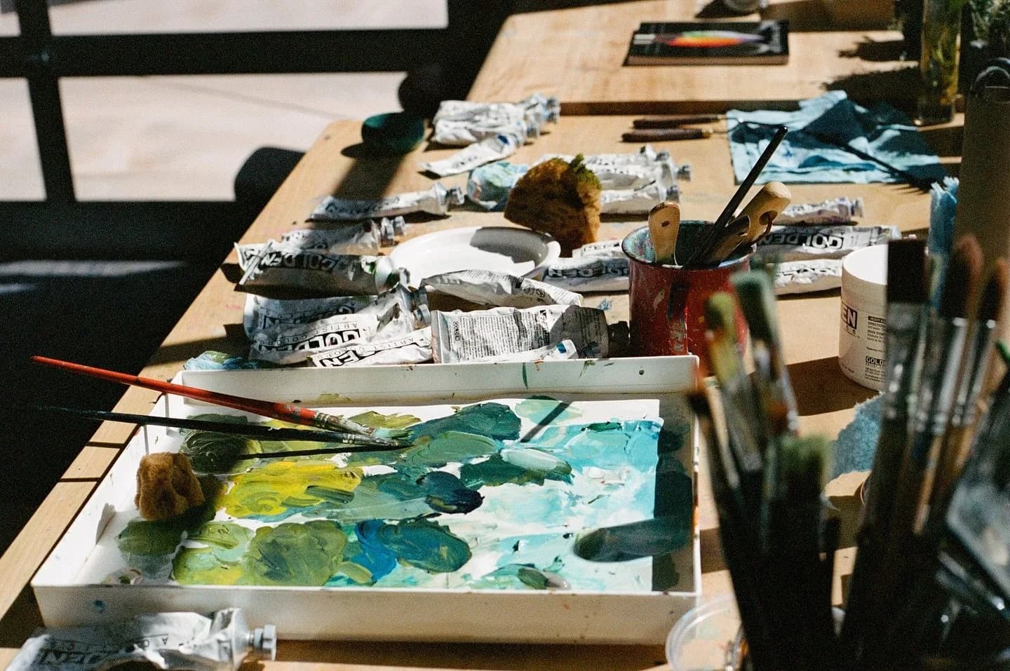 A palette of oil paints and brushes are laid out on a wooden table, ready for use.
