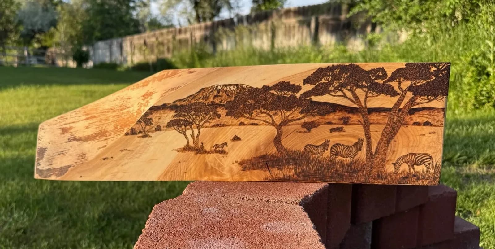 A wood burning depicts a savanna landscape with zebras and acacia trees against a mountain backdrop.