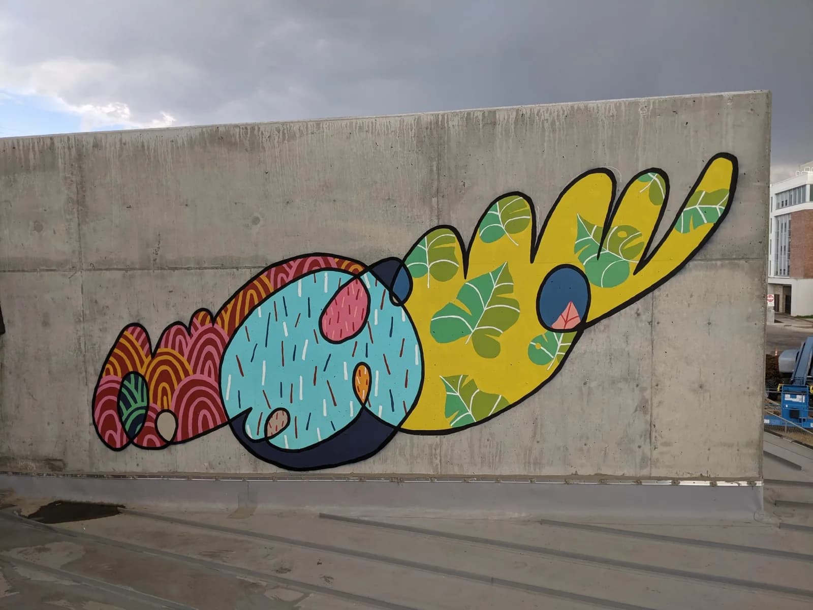 A vibrant abstract mural with organic shapes and patterns is painted on a concrete wall.