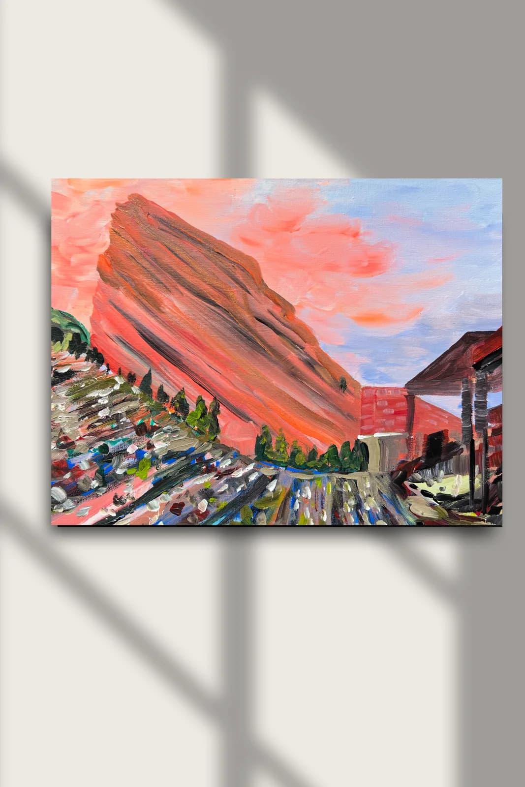 An impressionistic oil painting depicts the iconic Red Rocks Amphitheatre with a vibrant sunset sky.