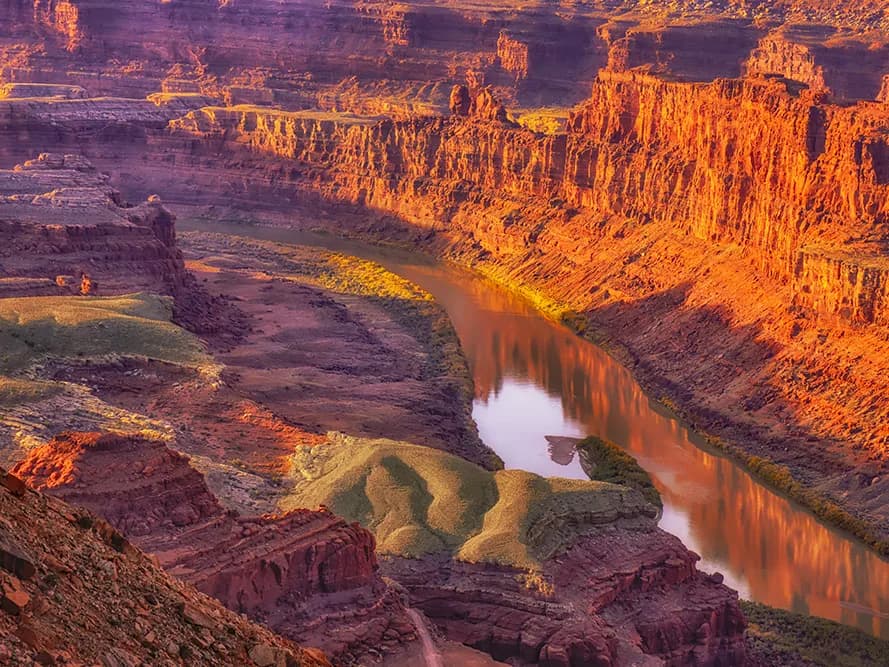 A dramatic landscape photograph captures a winding river through a canyon bathed in the warm glow of sunset.