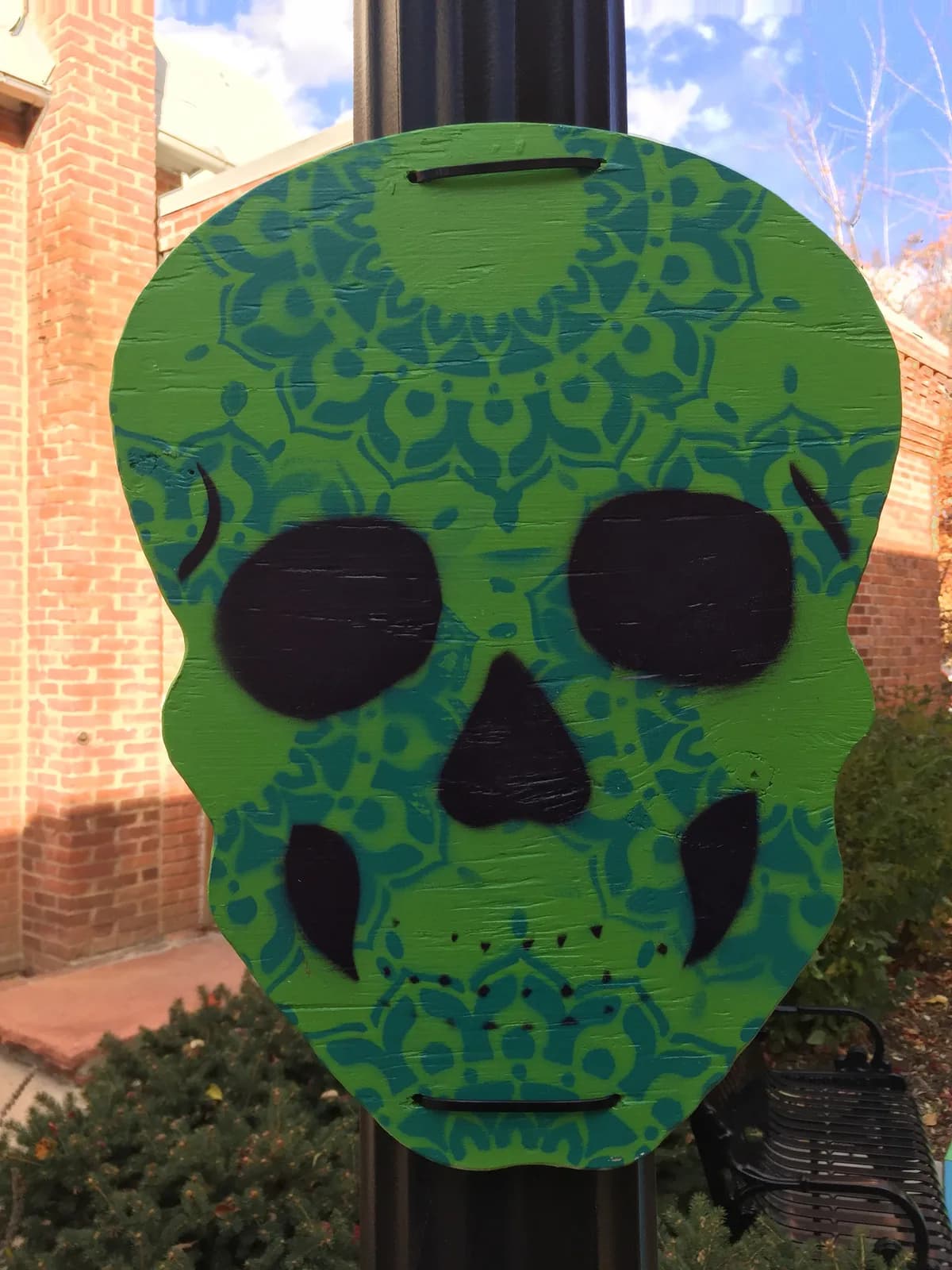 A green wooden skull decorated with a teal mandala pattern, painted in a folk style.