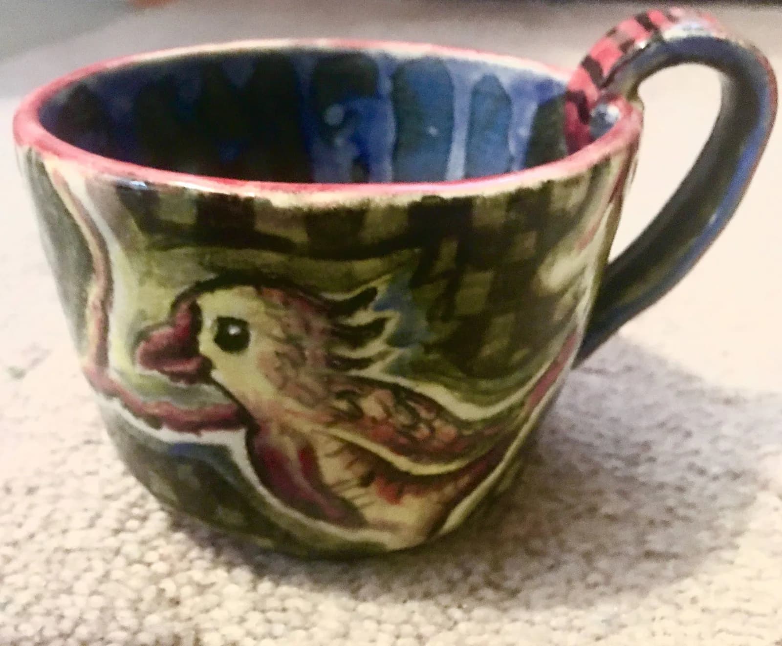 A hand-painted ceramic cup features a stylized bird design with vibrant blue and pink glazes.
