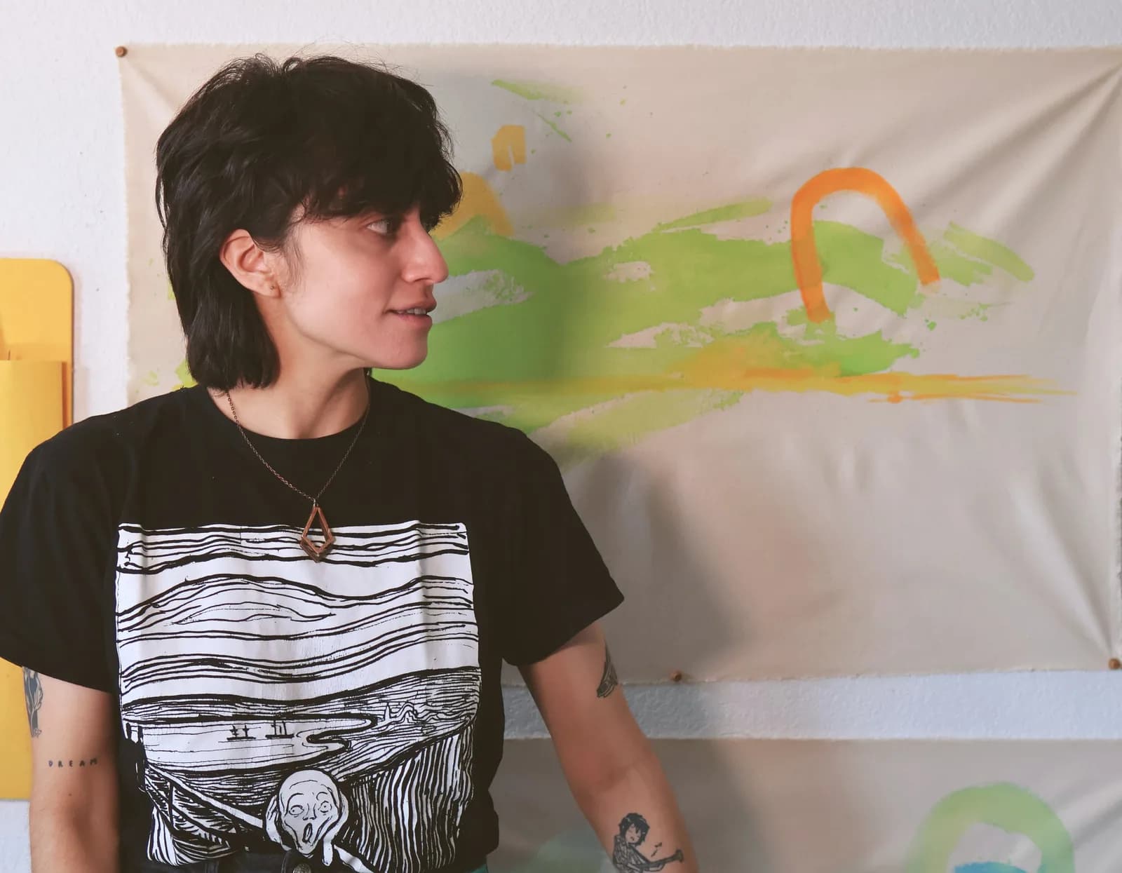 An abstract painting with green and orange hues is displayed on a wall behind a person wearing a t-shirt featuring "The Scream".