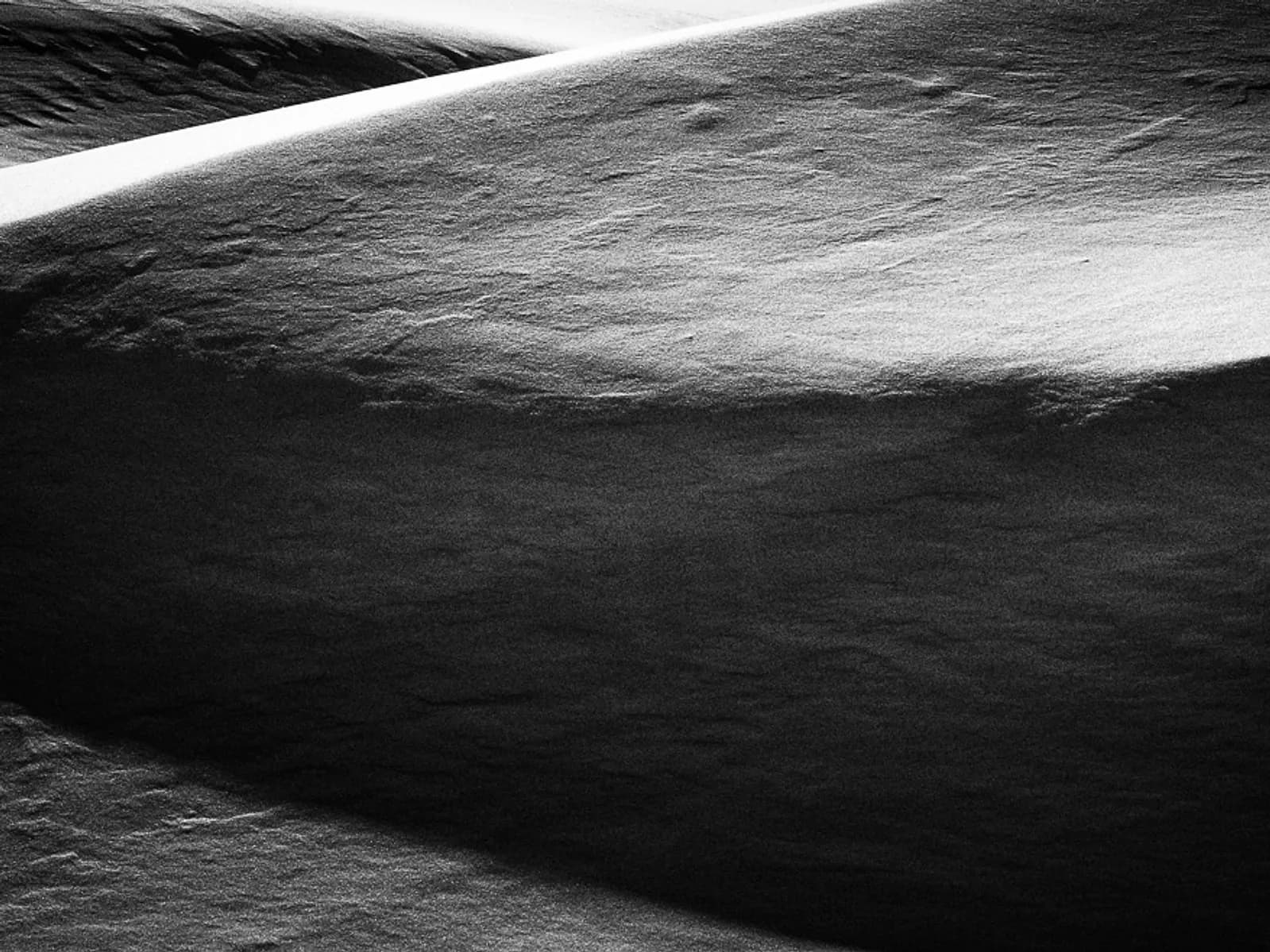 Abstract black and white photograph of snow dunes, emphasizing texture and light.