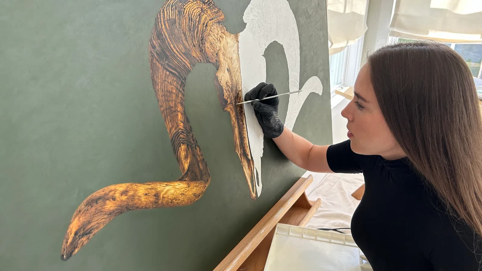 An artist works on a painting of a horn in a studio.