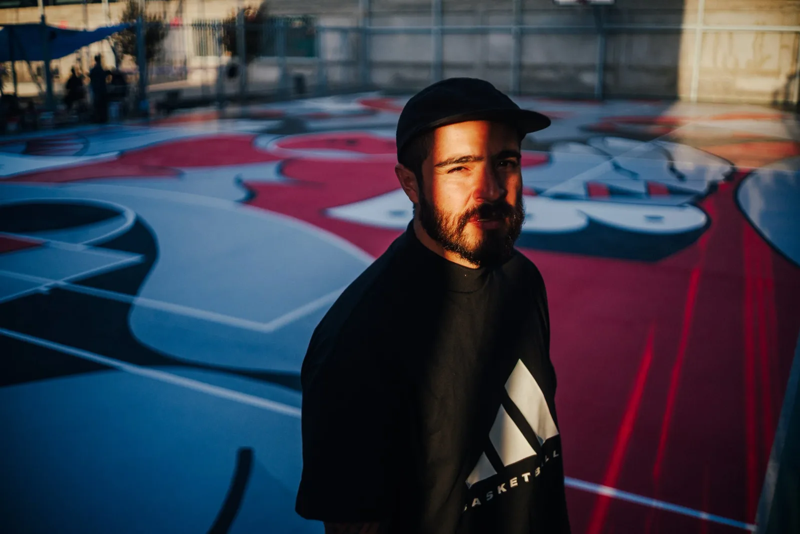Artist posing in front of a colorful basketball court mural with abstract designs in Tawny Port and Mirage.