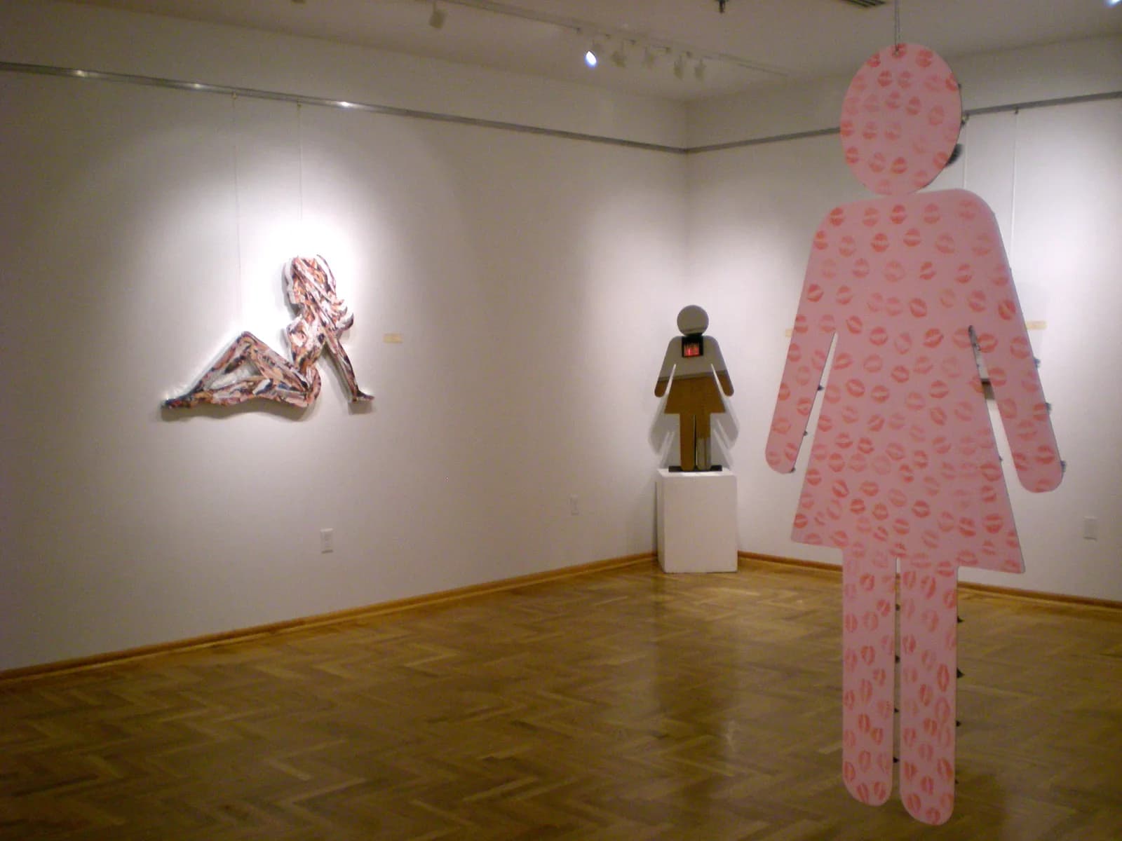 A large pink figure adorned with lip prints and a smaller figure in a gallery setting.