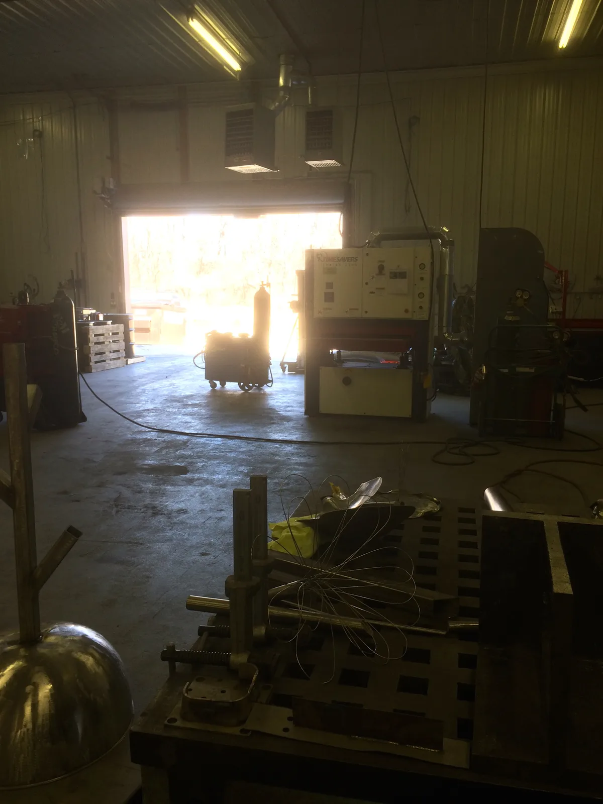 A metalworking studio with welding equipment and materials in the foreground and background.