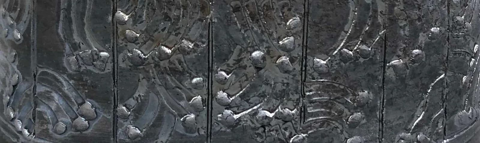 An abstract metal sculpture with a textured surface in shades of gray and Abbey.