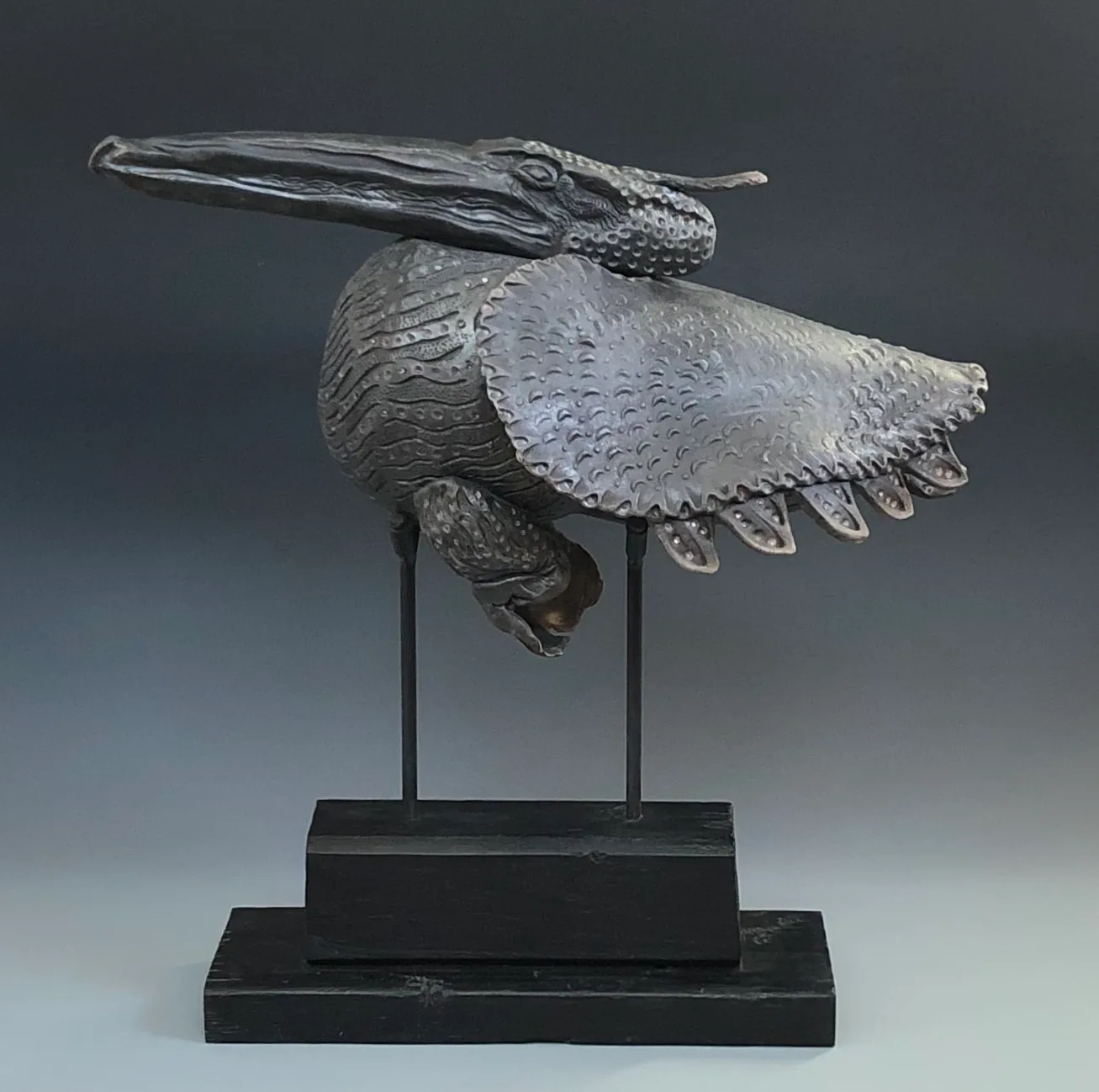 A metal sculpture of a pelican in flight, with intricate detailing on its wings and body.