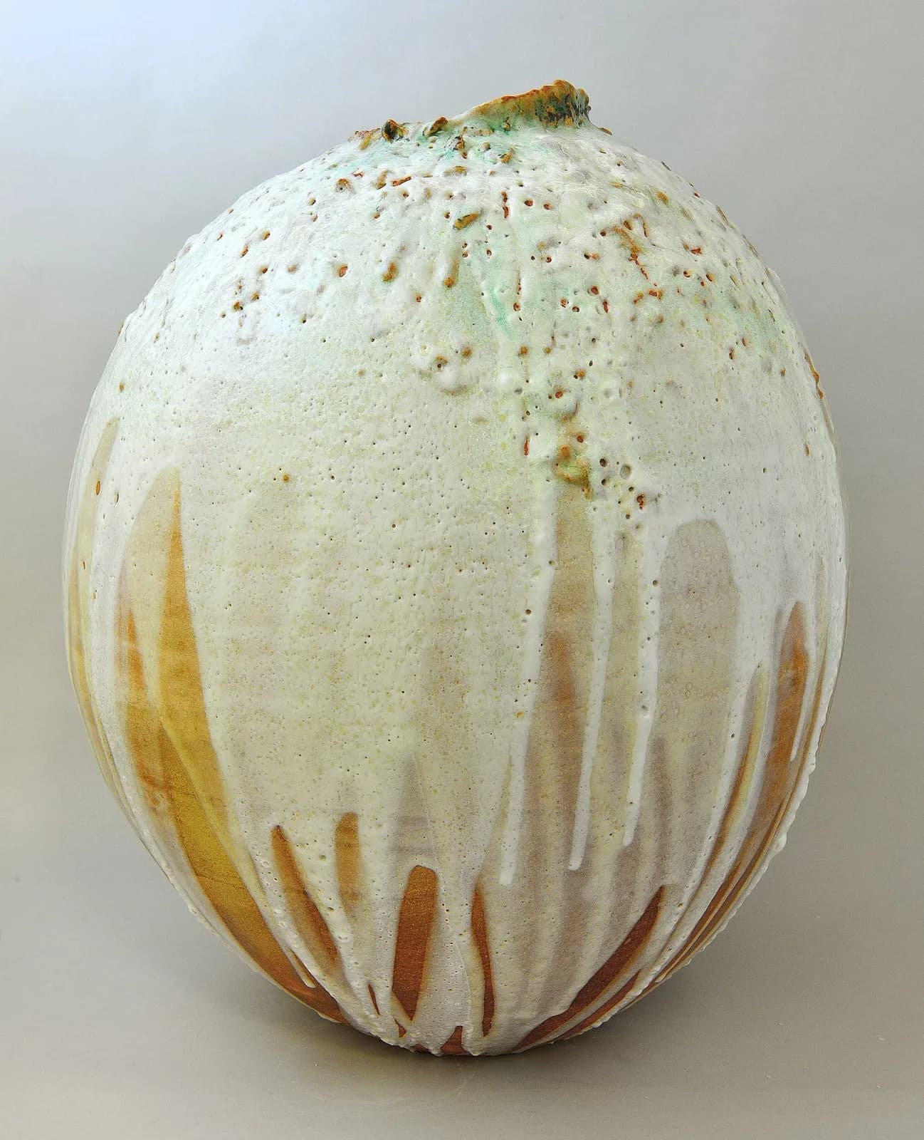 A textured ceramic vase with a drippy white and green glaze over a warm golden base.