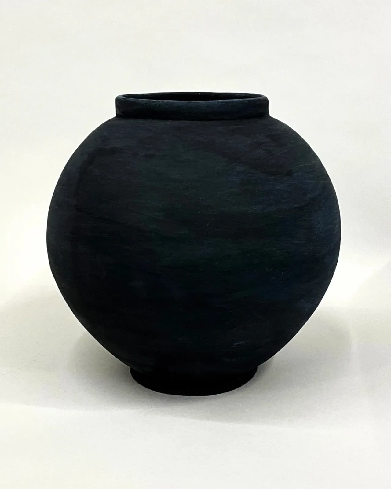 A dark ceramic vase with a textured surface, presented against a white background.