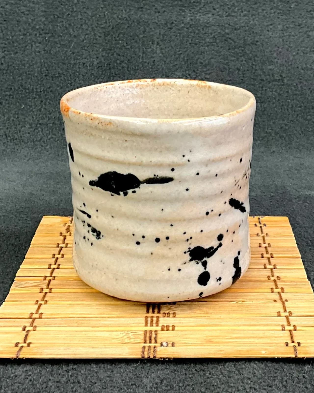 A speckled ceramic cup with a rough texture and a rustic glaze sits on a bamboo mat.