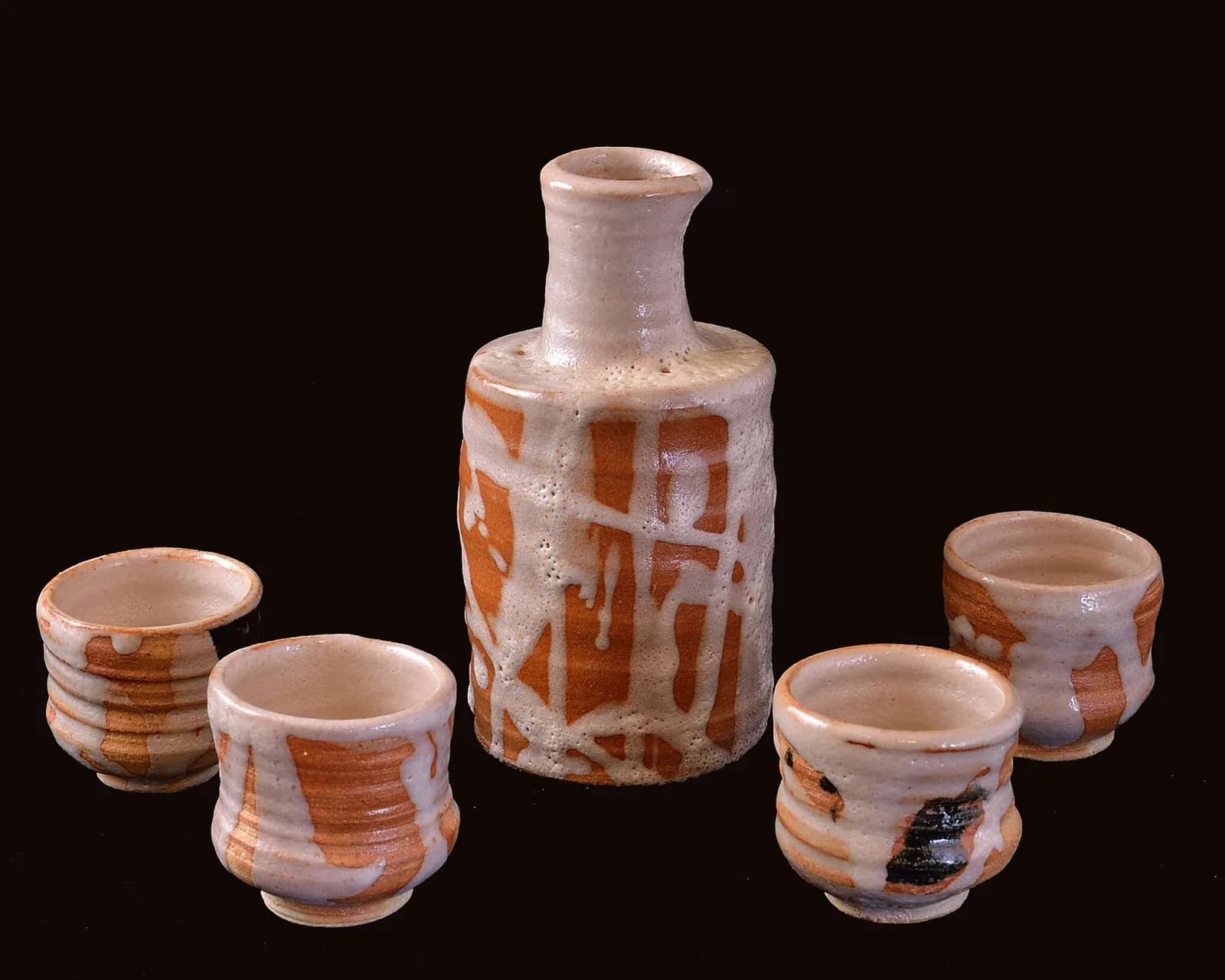 A ceramic sake set with a bottle and four cups, featuring a glaze with toast and asphalt tones.