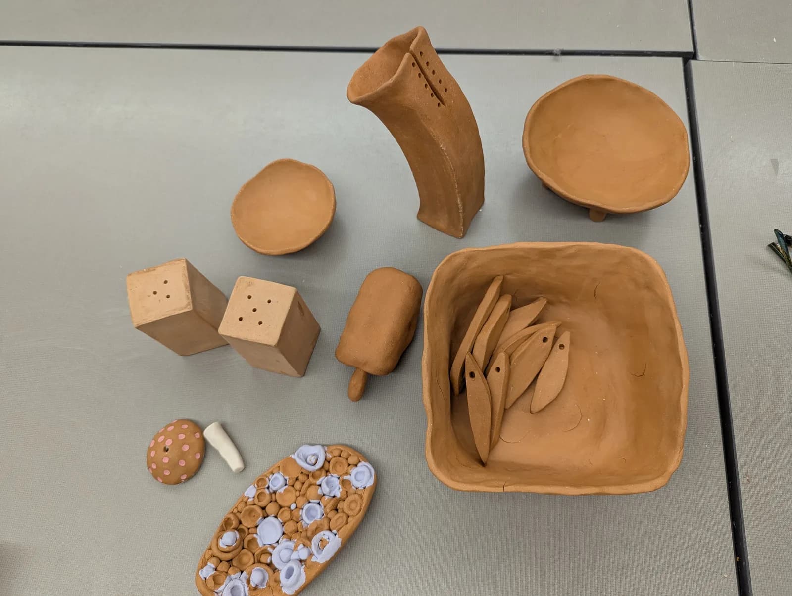 Various unfired clay ceramic pieces including salt shakers, bowls, and decorative objects.