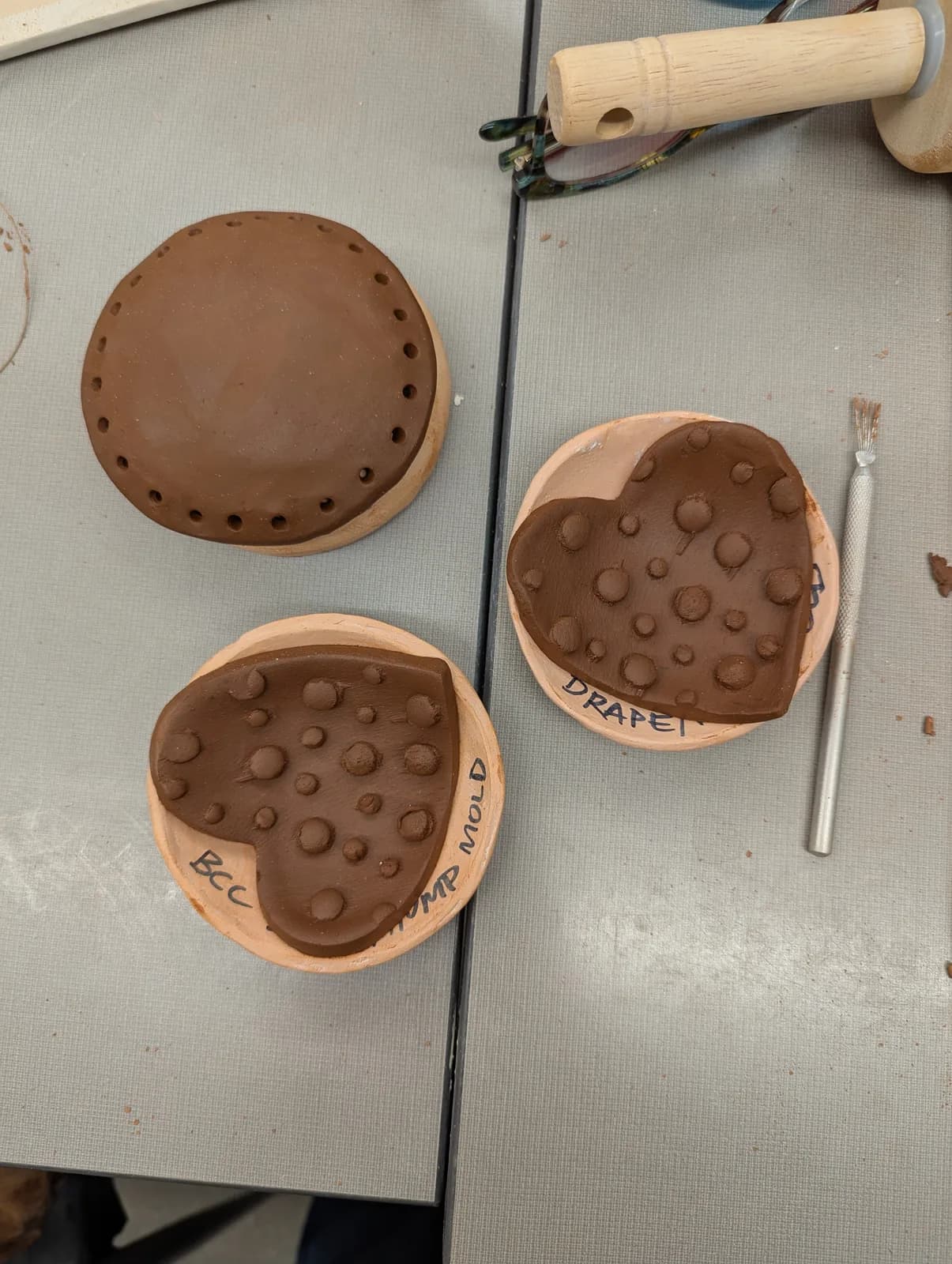 Clay molds in heart and circular shapes with textured surfaces and perforations.