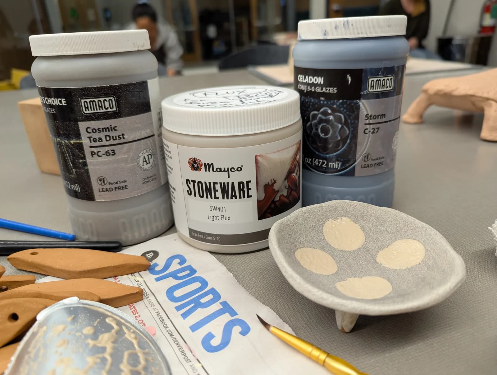 Ceramic art supplies including glazes and tools are arranged on a table in a studio setting.