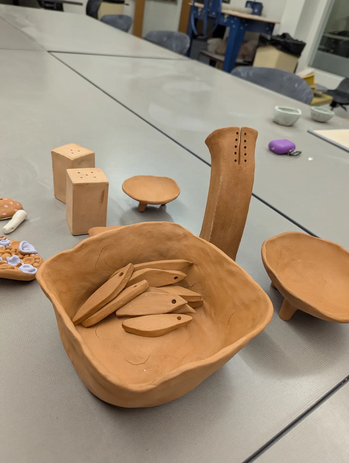 Unfinished clay pottery pieces, including a bowl with fish-shaped elements, sit on a studio table.