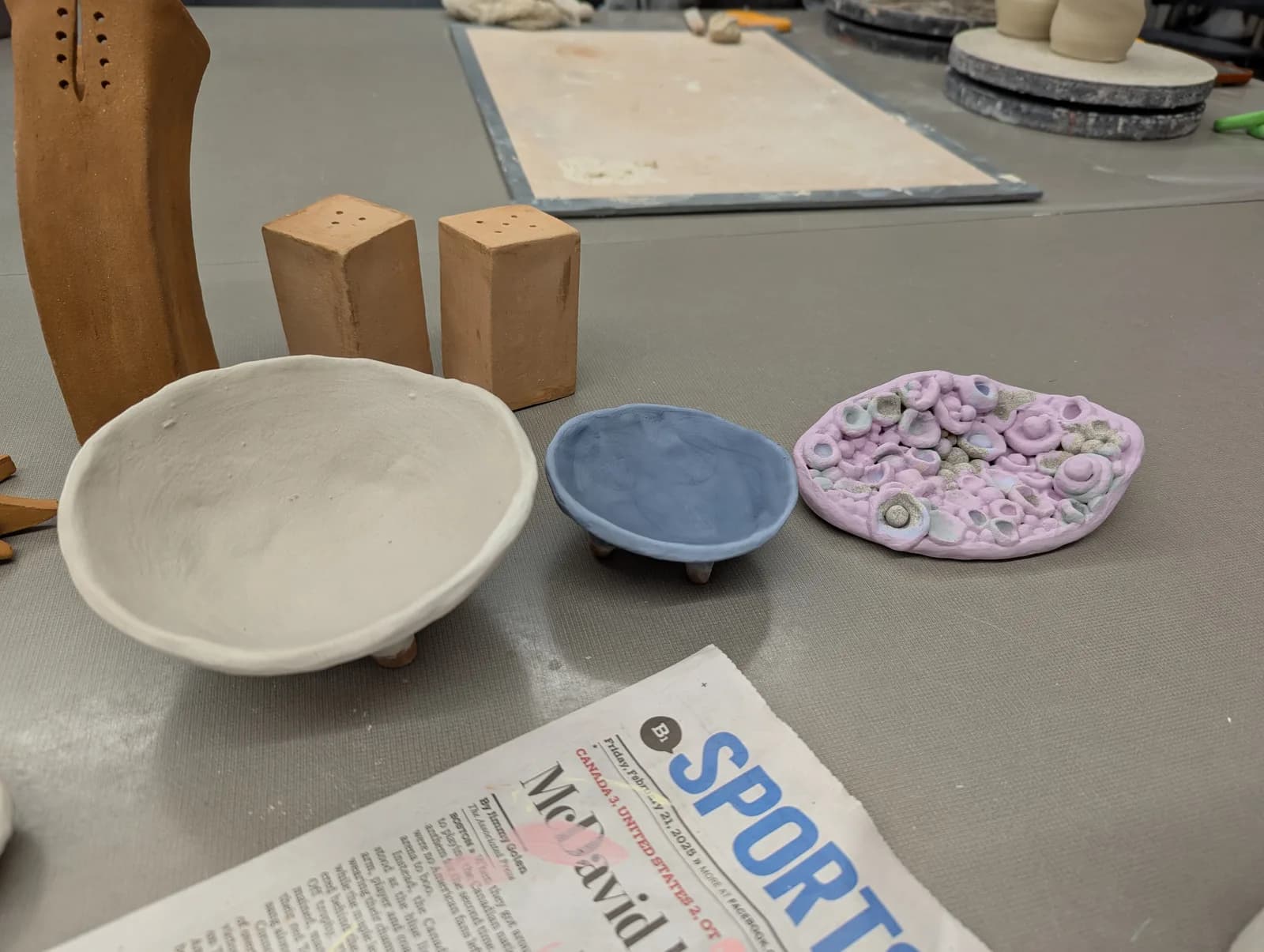 A collection of unfired clay pottery pieces in various stages of completion on a studio table.