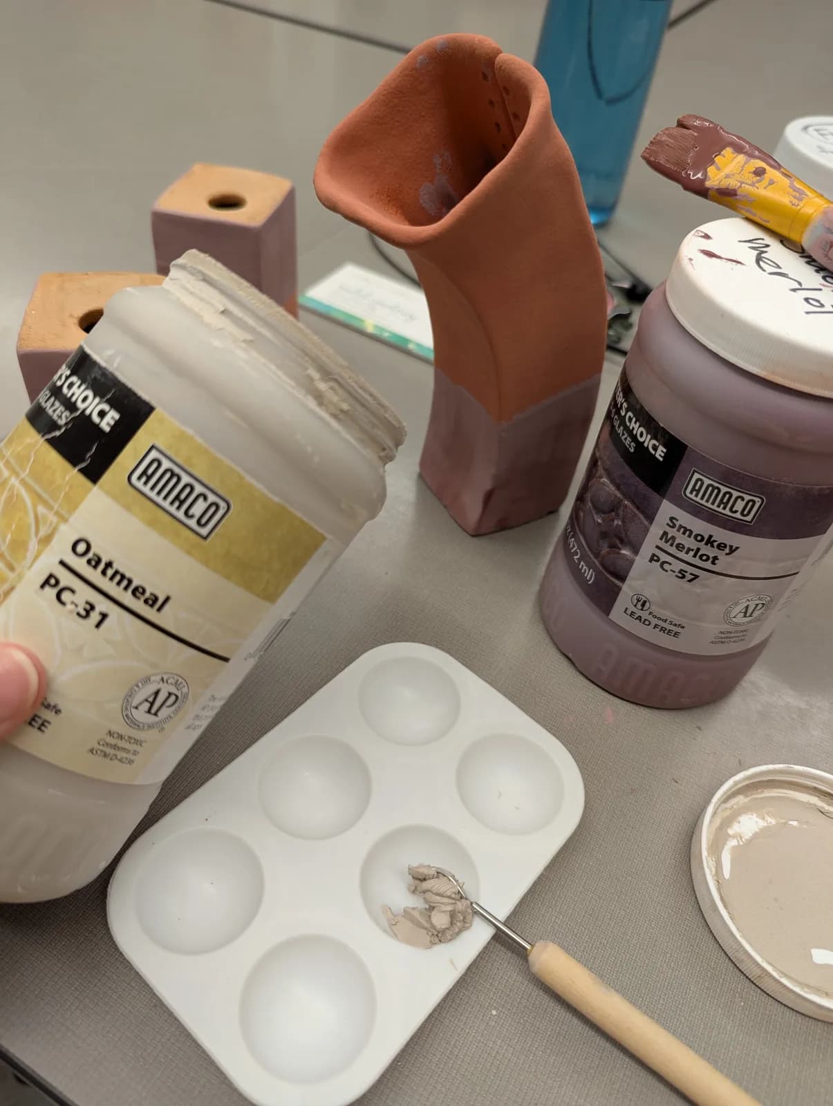 A ceramic artist's studio setup with glazes, tools, and unfinished pottery pieces.