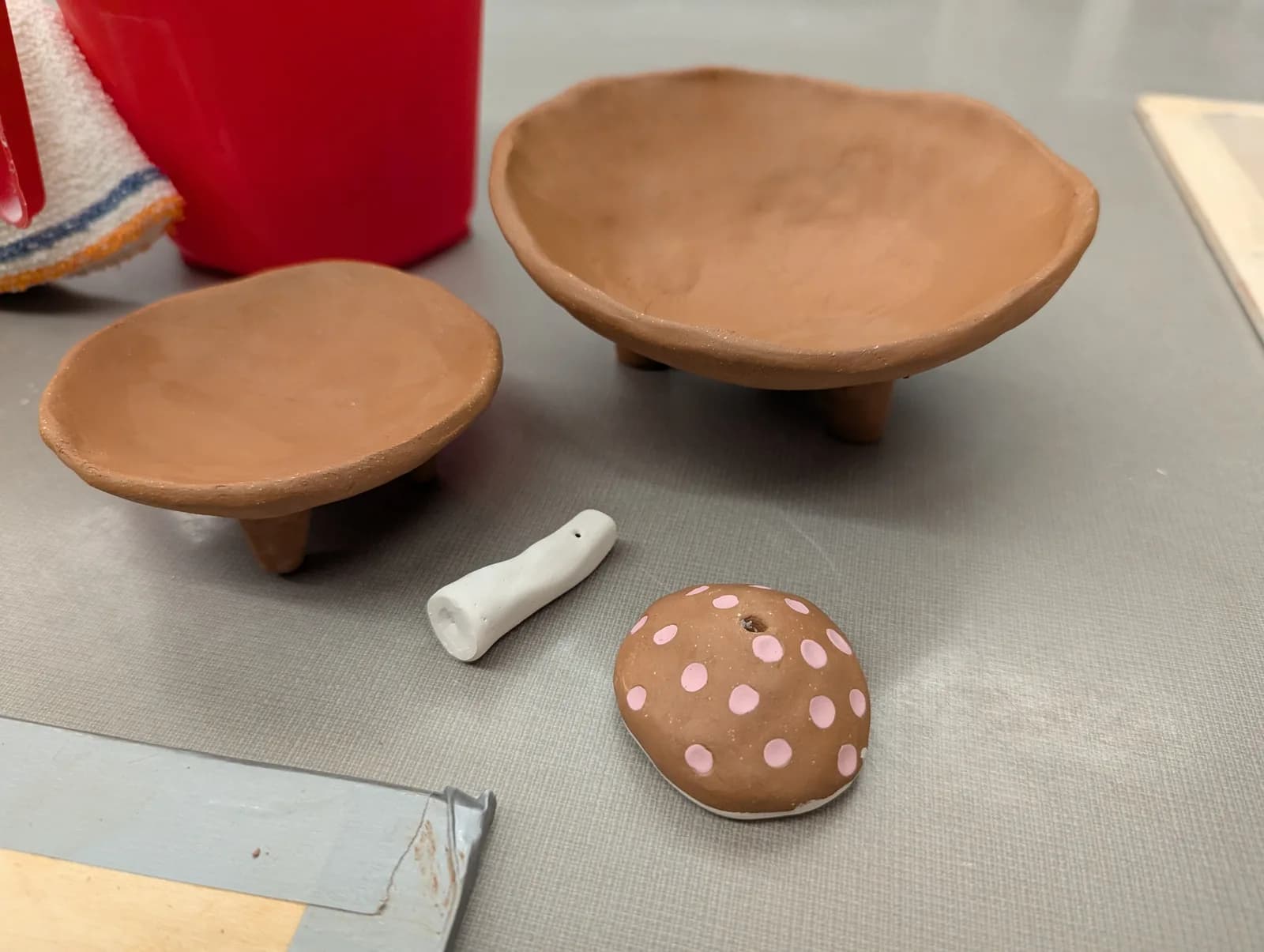 Unfinished clay pottery pieces including small bowls and decorative elements are displayed on a work surface.