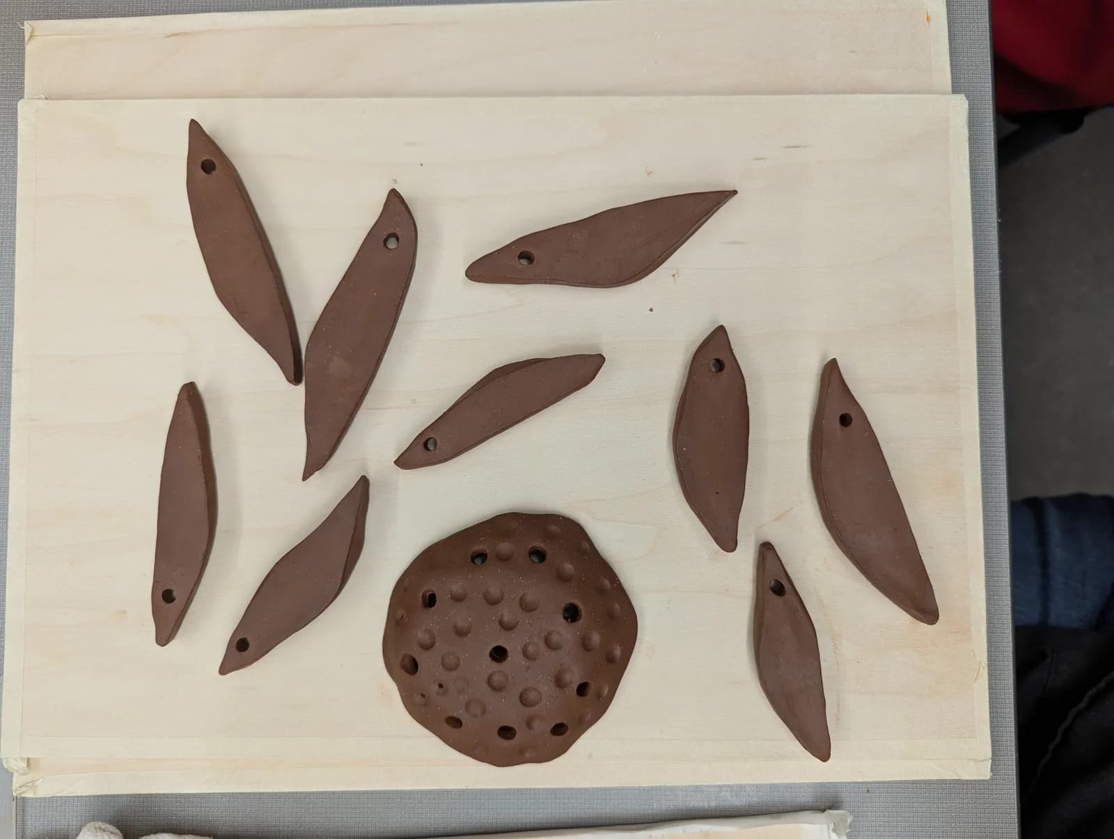 Clay pieces and tools are arranged on a wooden board, suggesting a pottery studio in progress.