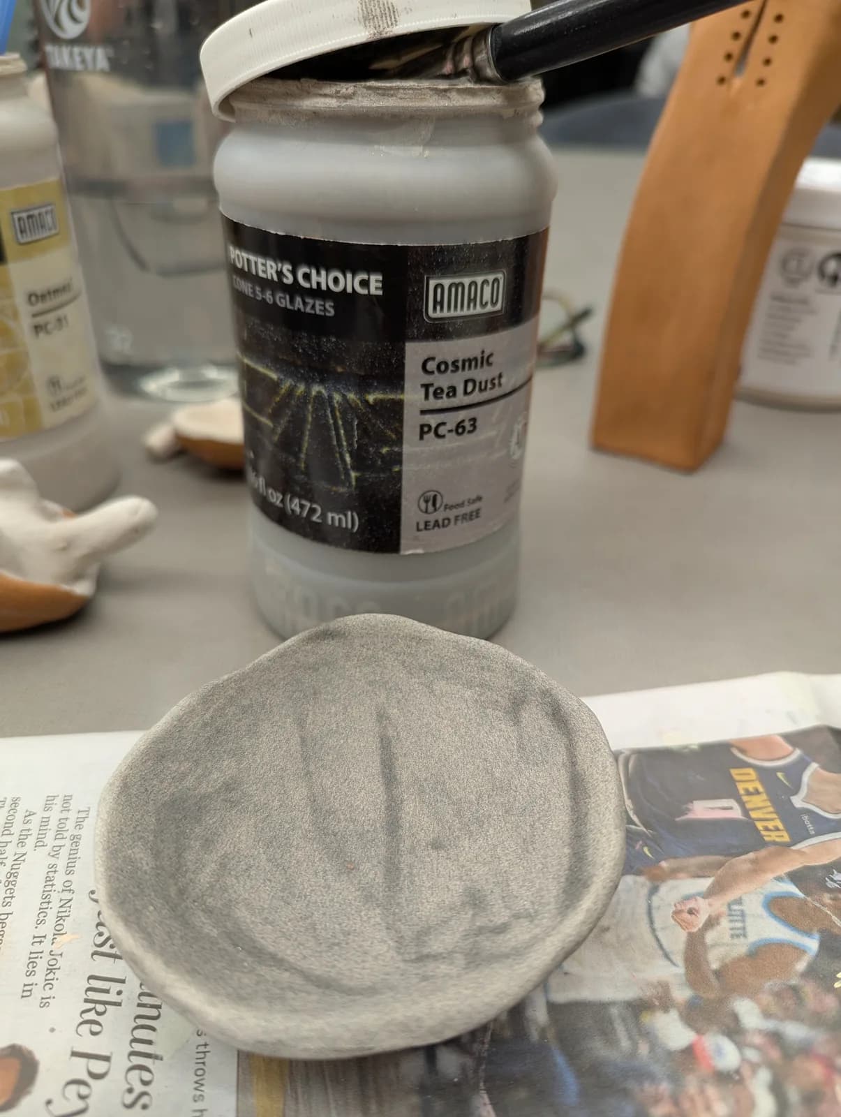 A ceramic piece in progress with a jar of Amaco Cosmic Tea Dust glaze and a brush.