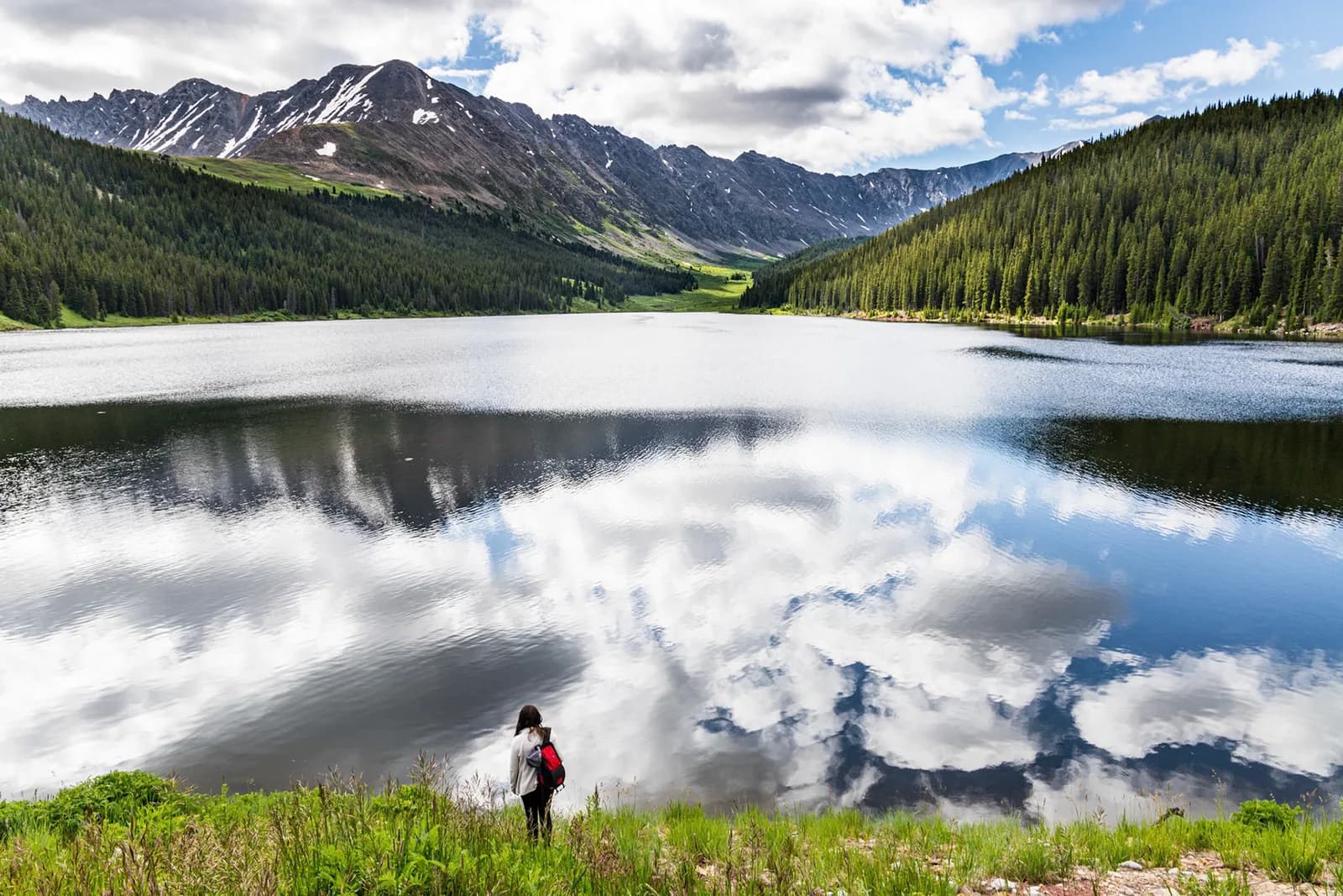 A serene landscape photograph captures a tranquil lake reflecting dramatic clouds and majestic mountains under a partly cloudy sky.