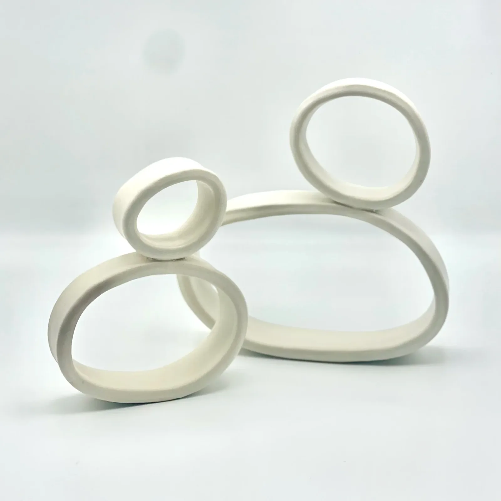 An abstract ceramic sculpture composed of interlocking rings and ovals in a matte white finish.