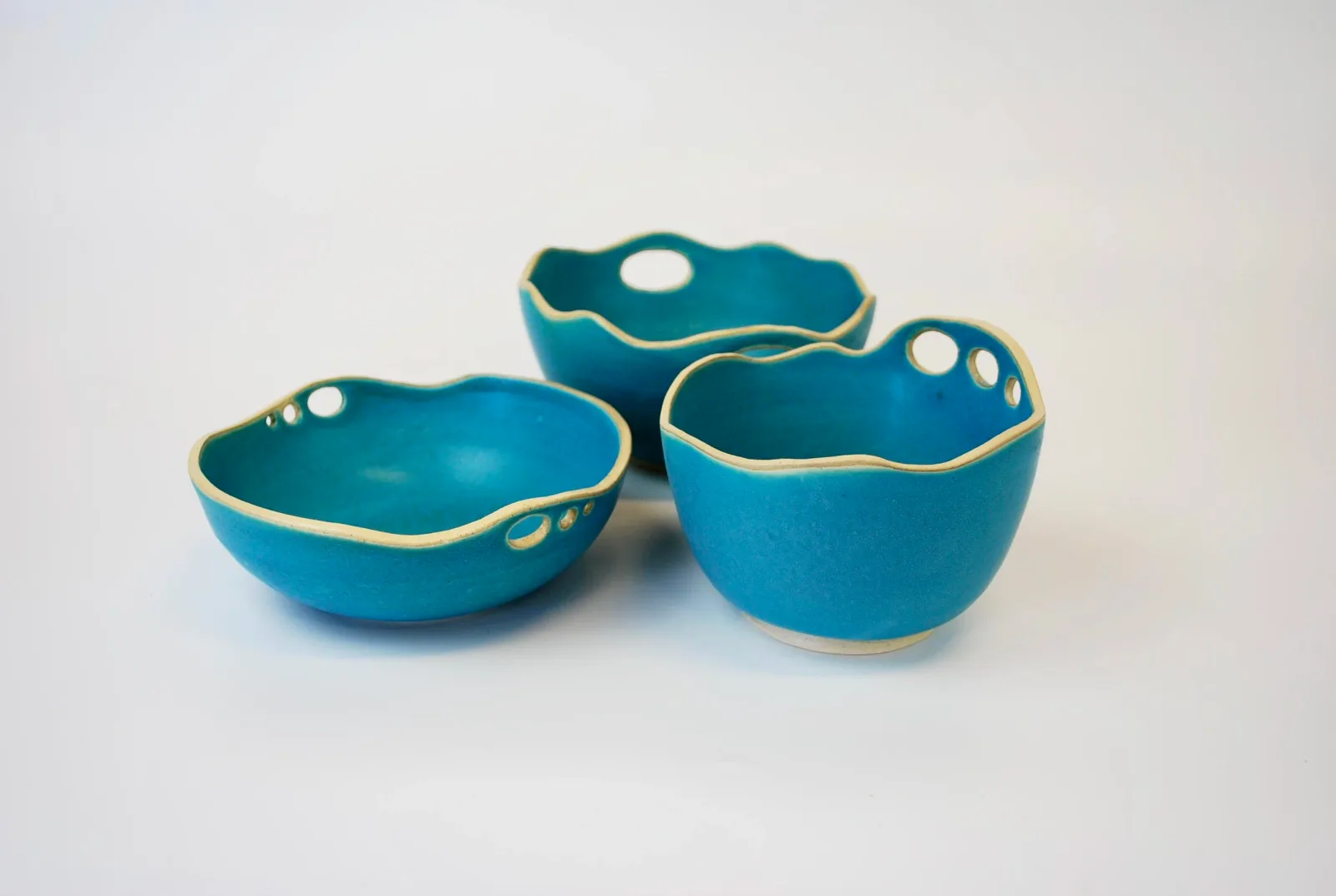 Three blue ceramic bowls with cut-out details and wavy rims are displayed on a white background.