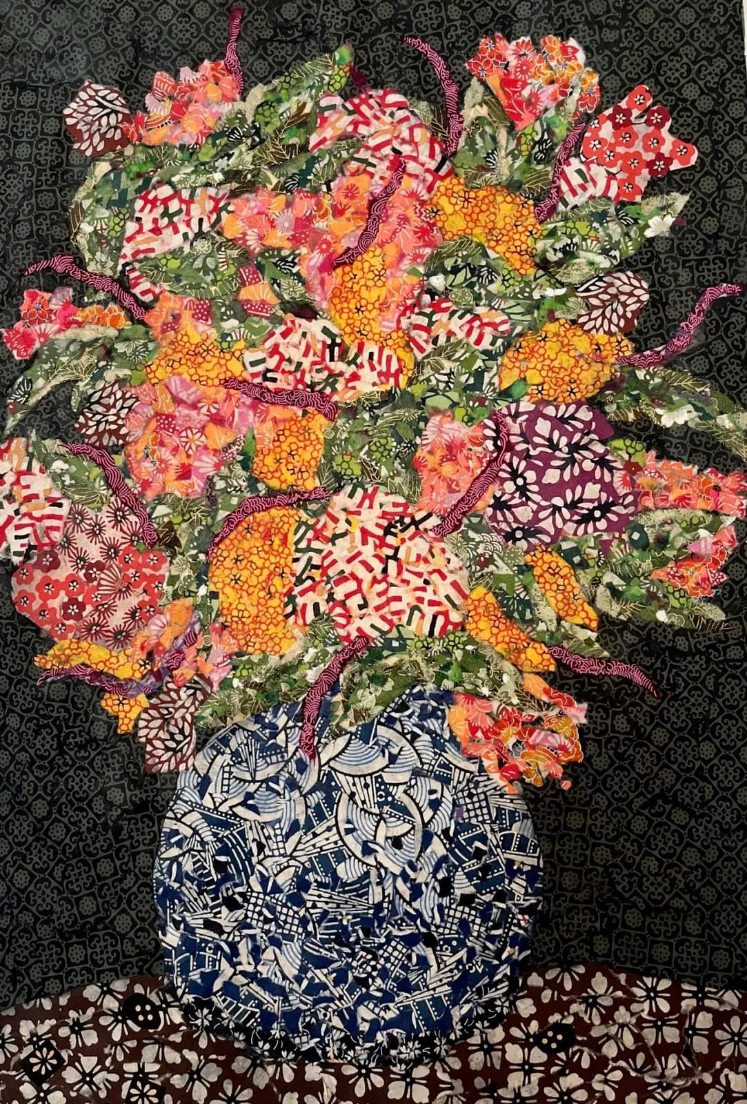 A fabric collage quilt depicts a vibrant floral arrangement in a patterned vase against a dark background.