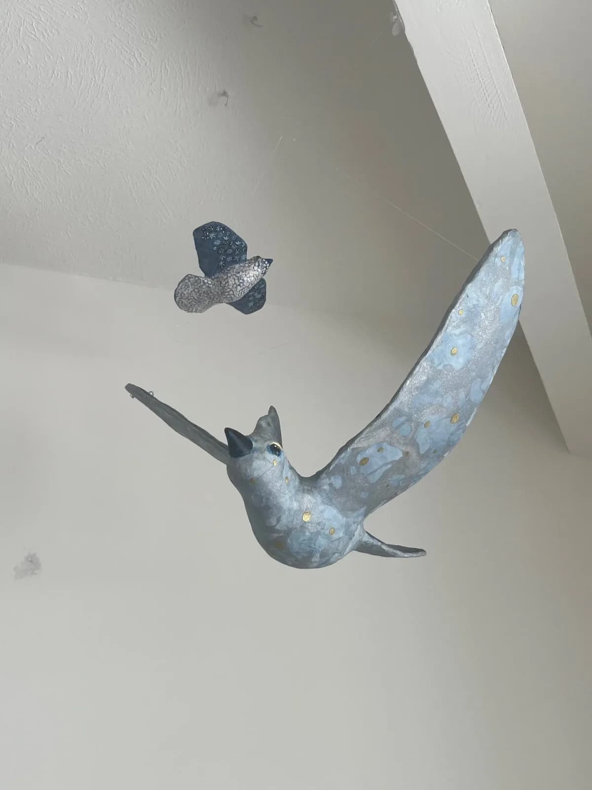 A metal sculpture of two birds in flight, rendered in shades of gray and accented with gold.