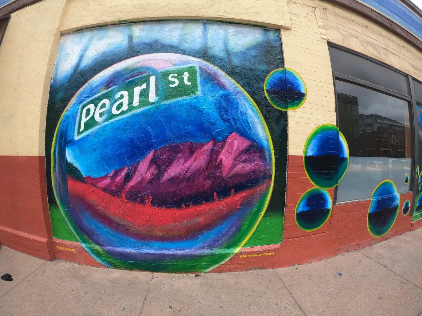 A vibrant mural depicts the Flatirons mountains within a bubble on Pearl Street, rendered in bold abstract style.