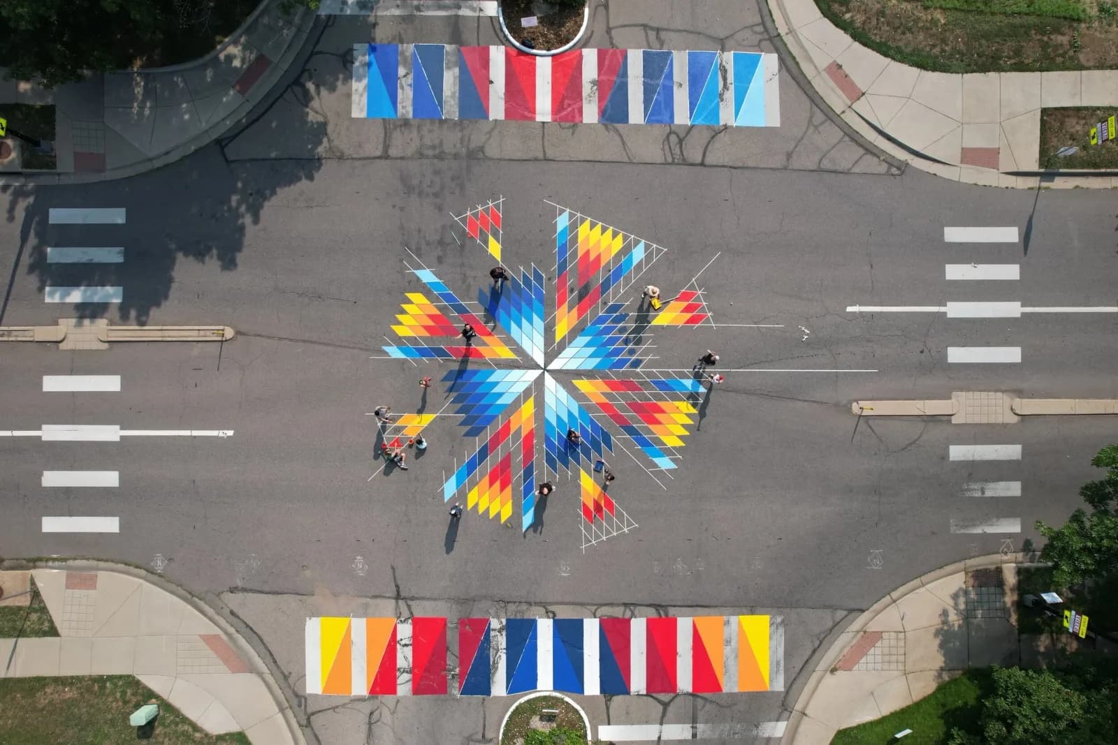 A vibrant geometric mural adorns a street intersection with colorful diamond shapes and lines.