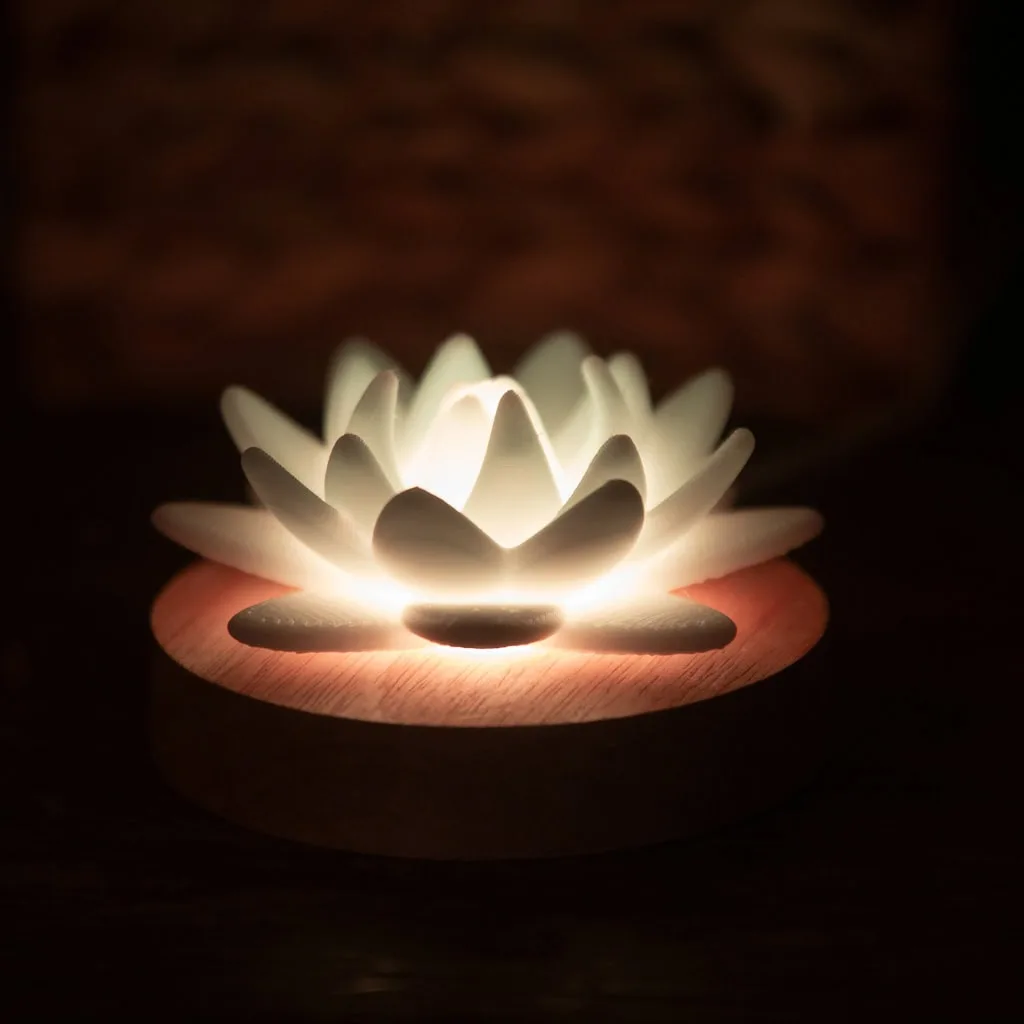 A ceramic lotus flower sculpture with an internal light source rests on a wooden base.