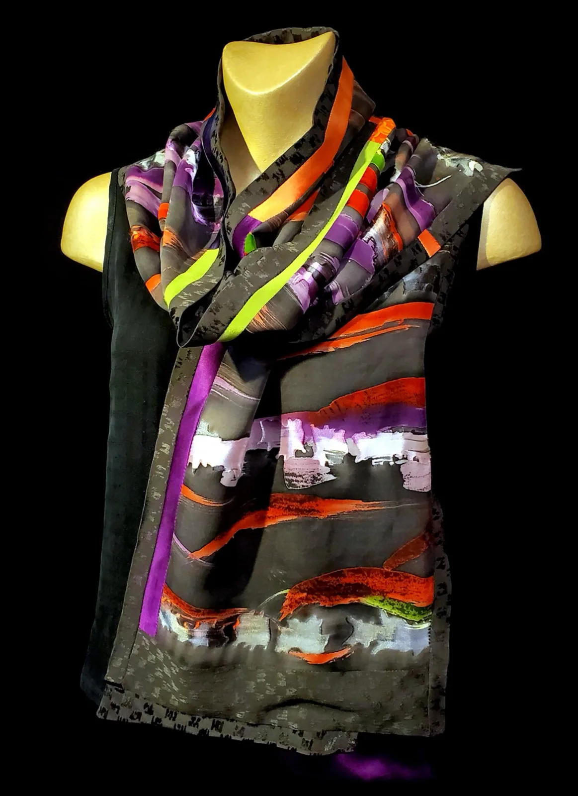 An abstract fiber art scarf features bold brushstrokes in plum, orange, and lime green on a dark background.